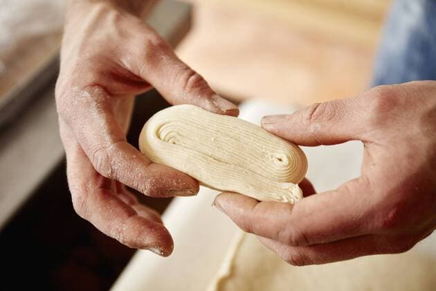 A baker holding dough which has been folded and worked to show the layers incorporated into the dough, to make light layered pastries. A baker holding dough which has been folded and worked to show the layers incorporated into the dough, to make light layered pastries.  18446
