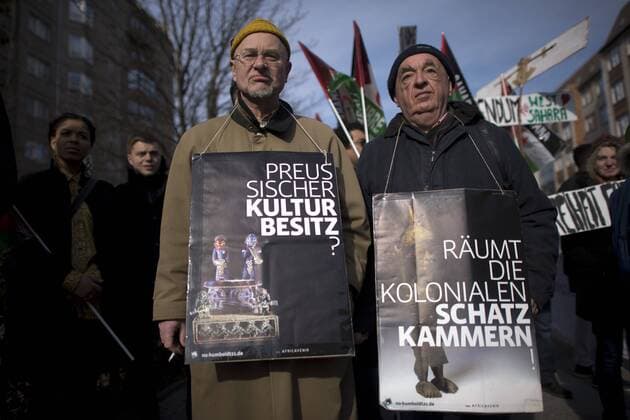Gedenkmarsch Kolonialgeschichte DEU, Deutschland, Germany, Berlin, 27.02.2016 Demonstrant mit Plakat Preussischer Kulturbesitz und raeumt die kolonialen Schatzkamamern gegen die Kolobialgeschichte und die Aneigung afrikanischer Kulturgueter durch deutsche Museen und dem Humboldt Forum beim 10. Gedenkmarsch zur Erinnerung an die afrikanischen Opfer von Versklavung, Kolonialismus und rassistischer Gewalt vom Komitee fuer ein afrikanisches Denkmal in Berlin und afrikanischer Vereine in Berlin. Dieser Gedenkmarsch wurde ins Leben gerufen, um der Forderung nach Anerkennung der Verbrechen gegen Schwarze Menschen und Menschen afrikanischer Herkunft Nachdruck zu verleihen. Anlass ist die Berliner Afrika-Konferenz von 1884 - 1885, auf der Afrika vor 130 Jahren unter den europaeischen Kolonialmaechten aufgeteilt wurde. Mehr als 30 Millionen Afrikanerinnen und Afrikaner wurden Opfer von Versklavung