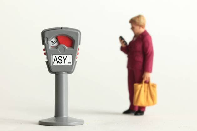 Symbolbild Bundeskanzlerin Dr Angela Merkel und ihre Asylpolitik: Miniatur Figur der Kanzlerin steht bei einer Parkuhr mit Wort Asyl und fast abgelaufener Parkzeit