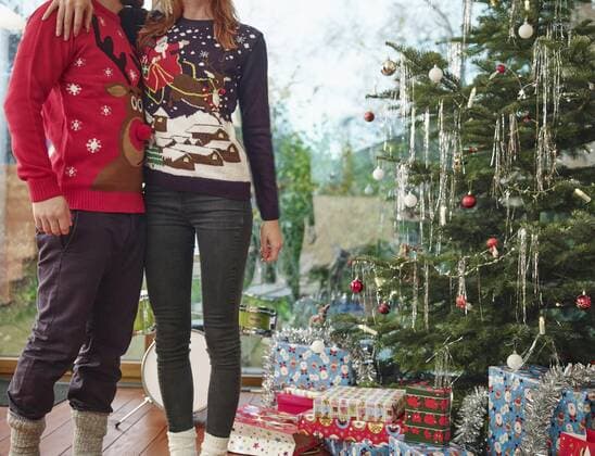 Couple standing in front of Christmas tree wearing Christmas jumpers model released Symbolfoto property released  RHF001326