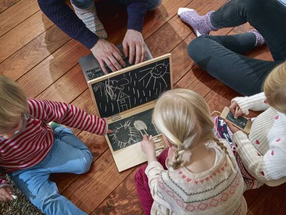 Father using laptop sitting on floor with daughters drawing on toy laptop model released Symbolfoto property released  RHF001340