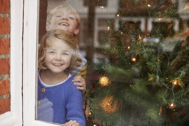 Two children, a boy and girl, looking out of a window at home beside a Christmas tree. Two children, a boy and girl, looking out of a window at home beside a Christmas tree.  20250