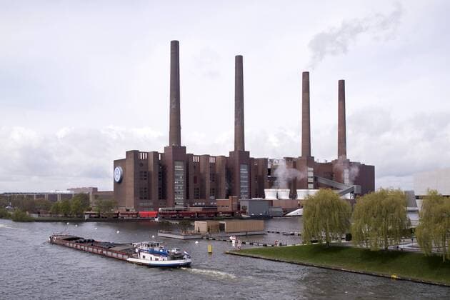 Volkswagen AG Deutschland, Germany, Wolfsburg, Niedersachsen, Lower Saxony, 28.04.2016 Lastkahn vor Schornsteine und Gebauede der Produktionshalle als Teil der Autostadt GmbH von der Volkswagen AG im Stammwerk Wolfsburg. VW versucht die aktuelle Krise um den Diesel-Manipulationsskandal und die damit verbundenen hohen Erstattungskosten zu ueberwinden. Building with chimney of the Volkswagen AG at the main production plant as part of the Autocity of the Car plant Volkswagen AG in Wolfsburg. The German carmaker VW tries to overcome its current crisis triggered by the engine-rigging scandal. Volkswagen is facing high costs and penalties, including the possible buyback of up to 500,000 cars alone in the USA, as a result of VW s diesel emissions scandal