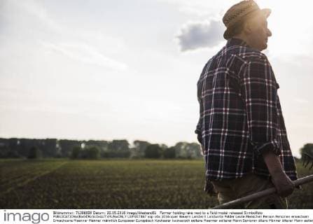 Farmer holding rake next to a field model released Symbolfoto  UUF007367