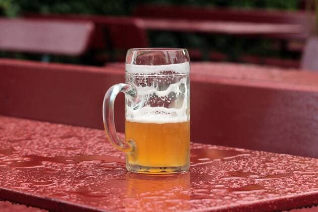 der bislang verregnete Sommer 2016 macht zumeist aus einem Biergartenbesuch ein nasses Unterfangen: Mass Bier steht auf einem regennassen Biertisch eines Biergarten s in Pfronten, Allgäu, Bayern, Deutschland