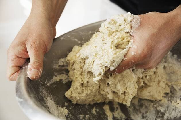 Close up of a baker kneading bread dough in a metal mixing bowl. Close up of a baker kneading bread dough in a metal mixing bowl.  21720