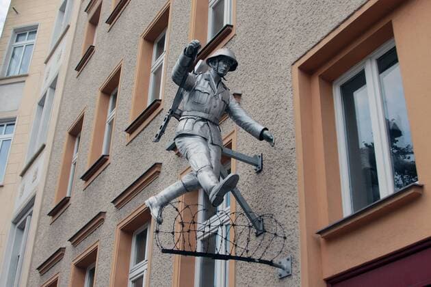 Gedenkstätte Bernauer Straße an der ehemaligen Mauer in Berlin, Deutschland: Skulptur des über den Stacheldraht springenden NVA Soldaten Hans Conrad Schumann an einer Hauswand