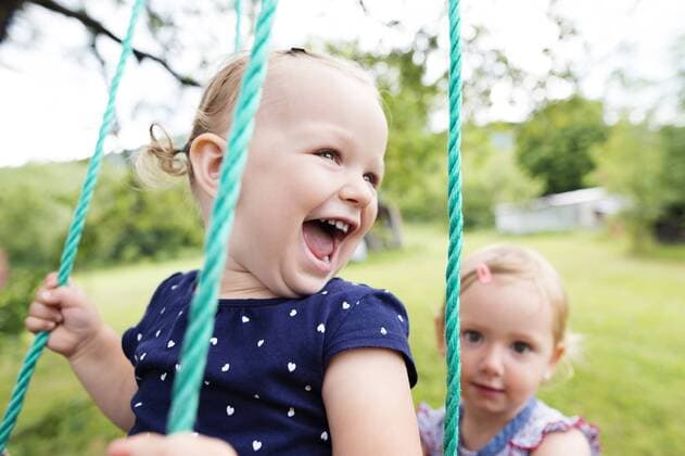 Laughing little girl on a swing with sister in the background model released Symbolfoto  HAPF000689