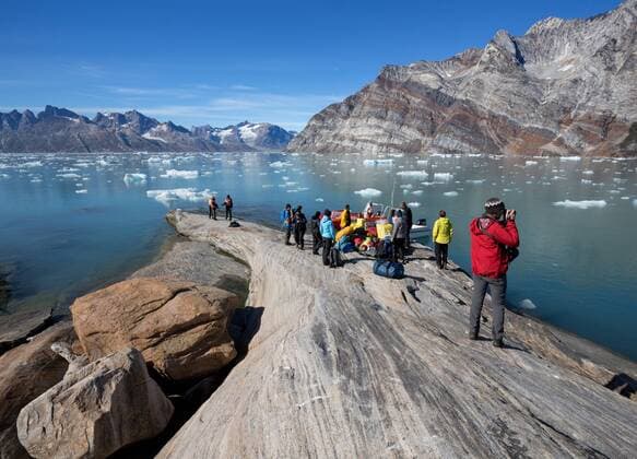 Europa; Skandinavien; Fjord; Wasser; Eis; Grönland; Ostgrönland: Touristengruppe beim Gepäck und Proviant verladen auf die Motorboote am Knud Rasmussen Gletscher vor Bergkulisse