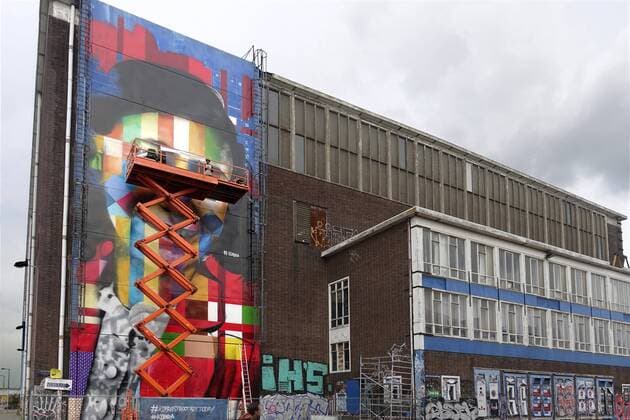 The Netherlands, Amsterdam. The famous Brazilian street artist Eduardo Kobra realizes this week a monumental portrait of Anne Frank, the man at the right side of the platform is Eduardo Kobra, 26 september 2016, Photo: Katrien Mulder Hollandse Hoogte Nederland, Amsterdam, Amsterdam Noord, NDSM Terrein, wereldberoende Braziliaanse streetartist Eduardo Kobra realiseert deze week een monumentaal portret van Anne Frank op de zuidelijke buitenmuur van de loods op de hoek van de MS van Riemsdijkweg, en de Tt Neveritaweg, , de man rechts in de hoogwerker is Eduardo Kobra 59396759
