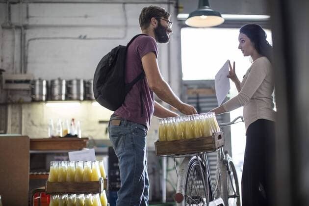 Delivery man with juice bottles on bicycle talking to woman in warehouse model released Symbolfoto property released  ZEF009918