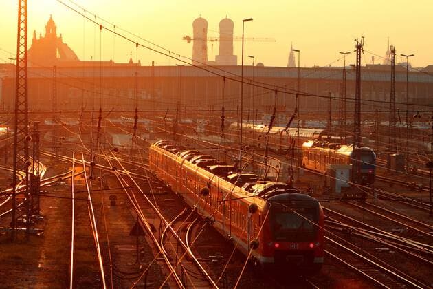 Hauptbahnhof München mit Gleisanlagen, Frauenkirche und einfahrendem Regional Express der DB Deutsche Bahn bei Sonnenaufgang, Bayern, Deutschland