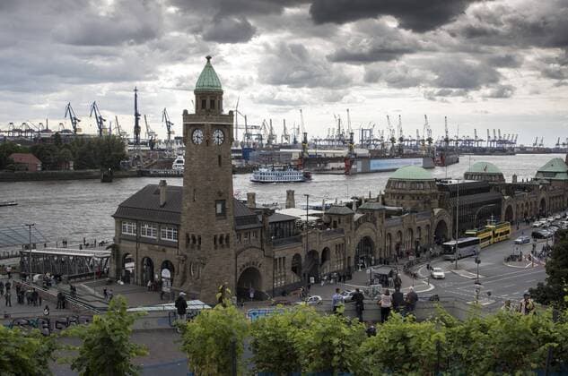 Dunkle Wolken über den historischen St. Pauli-Landungsbrücken. Sie liegen im Hamburger Stadtteil St. Pauli zwischen Niederhafen und dem ehemaligen Hamburger Fischmarkt an der Elbe in der Hansestadt Hamburg. Bei den Landungsbrücken handelt es sich um eine große Anlegestelle für Fahrgastschiffe am Nordrand des Hamburger Hafens. An ihrem westlichen Ende befindet sich der nördliche Eingang zum Alten Elbtunnel. Den östlichen Abschluss des Gebäudekomplexes bildet der Pegelturm. Auf halber Höhe des Turmes auf der Elbseite ist oben in der Mauer ein Wasserstandsanzeiger eingelassen, der über den aktuellen Stand der Tide informiert. In seiner zweiten Funktion ist der Pegelturm auch Uhren- und Glockenturm. Das Zifferblatt ist weithin sichtbar. Die Glocke erklingt zur vollen und halben Stunde. Im Hintergrund die Kräne des Hamburger Hafens. Landungsbrücken in St. Pauli