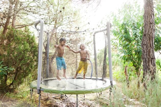 Two little boys jumping on trampoline while splashing with water from garden hose model released Symbolfoto  VABF00788