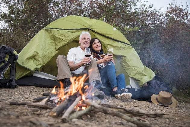 Happy senior couple sitting at campfire with wine at a tent model released Symbolfoto  ONF01049