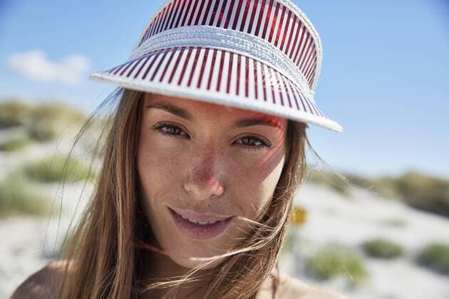 IMAGO Creative, Jahreszeit Sommer, Sonnenschutz Portrait of smiling young woman wearing sun visor on the beach model released Symbolfoto  SRYF000054
