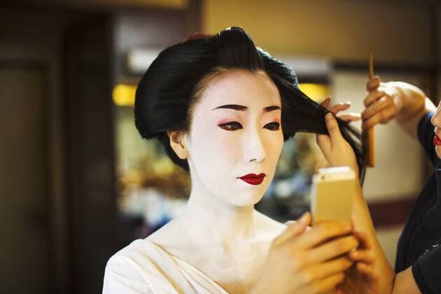IMAGO Creative: Kollidierende Kulturen A modern geisha or maiko woman being prepared in traditional fashion, with white face makeup. A modern geisha or maiko woman being prepared in traditional fashion, with white face makeup.  24872