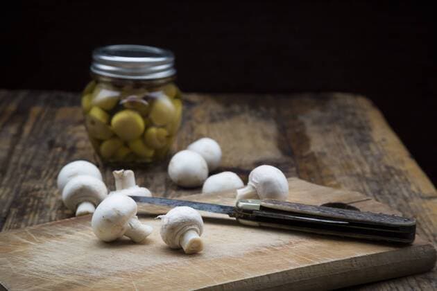 Fresh white champignon and pocket knife on wooden board and glass of pickled champignons  LVF05554