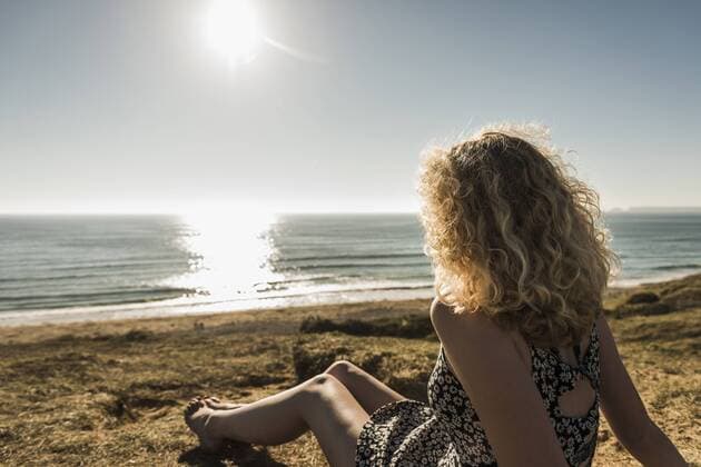 Back view of teenage girl sitting on the beach at evening twilight looking to the sea model released Symbolfoto UUF08741