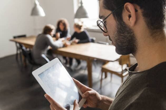 Young man using digital tablet in modern office with coworkers at table in background model released Symbolfoto property released  TCF05283