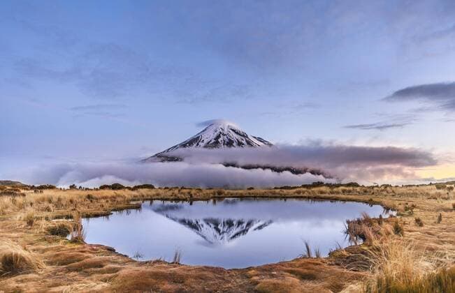 IMAGO Nature: Unsere Erde, Naturschutz, Naturschutzgebiete in Ozeanien Spiegelung im Pouakai Tarn Bergsee, Wolken um Stratovulkan Mount Taranaki oder Mount Egmont bei Sonnenuntergang, Egmont National Park, Taranaki, Neuseeland, Ozeanien Copyright: imageBROKER/MoritzxWolf ibxmmw04481960.jpg