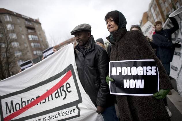 Gedenkmarsch Kolonialgeschichte DEU, Deutschland, Germany, Berlin, 25.02.2017 Demonstranten mit Plakat Apologise now, Entschuldigung sofort, Transparent Mohrenstrasse wegen Rassismus geschlossen fuer die Umbennenung von Strassennamen beim 11. Gedenkmarsch zur Erinnerung an die afrikanischen Opfer von Versklavung, Kolonialismus und rassistischer Gewalt vom Komitee fuer ein afrikanisches Denkmal in Berlin und afrikanischer Vereine in Berlin. Dieser Gedenkmarsch wurde ins Leben gerufen, um der Forderung nach Anerkennung der Verbrechen gegen Schwarze Menschen und Menschen afrikanischer Herkunft Nachdruck zu verleihen. Anlass ist die Berliner Afrika-Konferenz von 1884 - 1885, auf der Afrika vor 130 Jahren unter den europaeischen Kolonialmaechten aufgeteilt wurde. Mehr als 30 Millionen Afrikanerinnen und Afrikaner wurden Opfer von Versklavung und kolonialen Verbrechen gegen die Menschlichkeit.