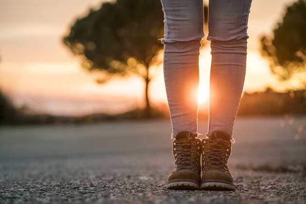 Woman wearing hiking boots standing on a road at sunset model released Symbolfoto  KKAF00443