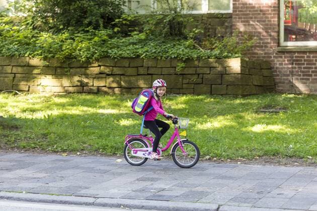 Smiling little girl with school bag riding bicycle on pavement model released Symbolfoto  JFEF00838