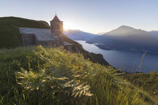 Sunbeam on Church of San Bernardo lights up the landscape around the blue water of Lake Como at dawn, Musso, Lombardy, Italy, Europe Copyright: RobertoxMoiola 1179-1503