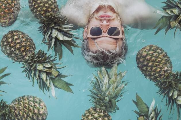 Young man in swiming pool surrounded by pineapples model released Symbolfoto  RTBF00747