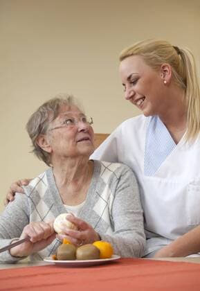05.12.2011, Deutschland - Generationen im Dialog. In der Tagesklinik einer Geriatrie wird eine Patientin bei Alltagsuebungen betreut von einer jungen Frau im sozialen Freiwilligendienst, FSJ Freiwilliges Soziales Jahr. Die angehende Krankenpflegerin unterstuetzt die Seniorin beim Apfelsine schaelen. Gestelltes Foto zum Thema Generationen im Dialog.