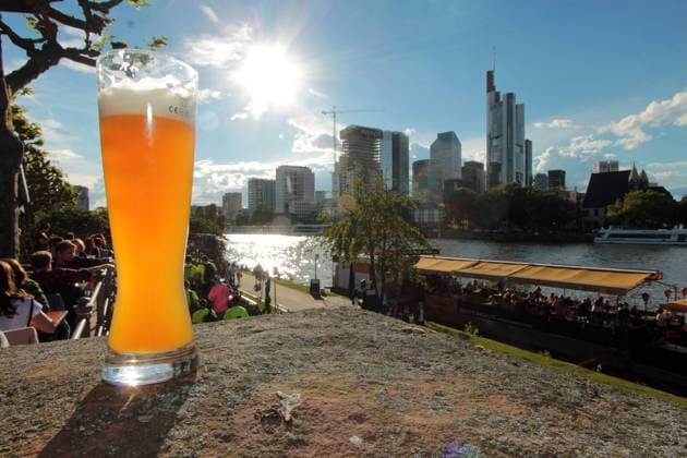 Frühlingswetter in Frankfurt, Hessen, Deutschland: Weißbier steht bei warmen Temperaturen am Mainufer vor der Skyline des Bankenviertel s in der Innenstadt