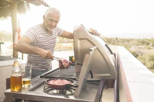 Mature man grilling steaks on a gas grill on his penthouse terrace model released Symbolfoto property released  ABAF02158
