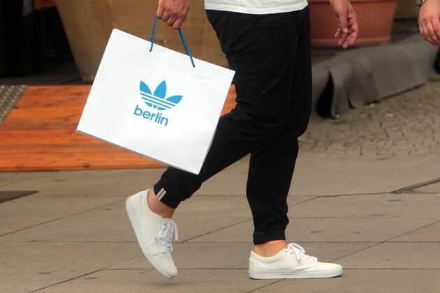 Mann trägt eine Papiertüte mit Emblem des Sportartikel Hersteller s Adidas in der Innenstadt Berlin, Deutschland