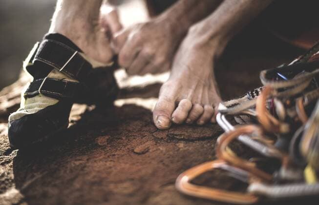 Close up of a free climber putting on rock climbing shoes with a pile of carabiners and rope. Close up of a free climber putting on rock climbing shoes with a pile of carabiners and rope.  29868