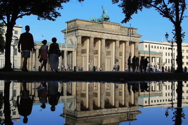Brandenburger Tor in Berlin spiegelt sich nach einem Regenschauer in einer großen Wasserpfütze bei strahlend blauem Himmel, Berlin, Deutschland