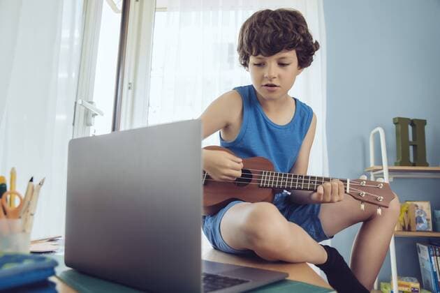 Boy using laptop to play a song on an ukulele model released Symbolfoto property released  MFF03792