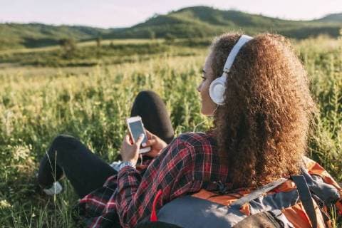 Teenage girl with backpack listening music with headphones on a meadow model released Symbolfoto  VPIF00118
