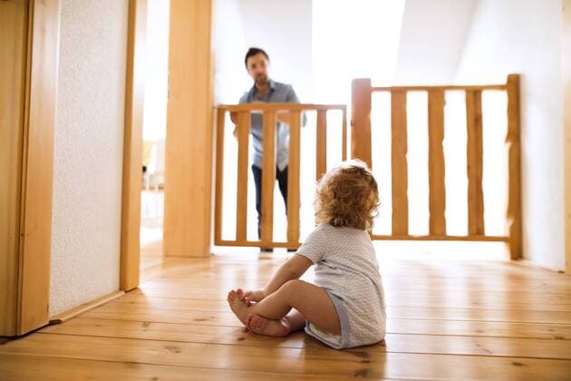 Baby boy sitting on wooden floor looking at father behind barrier at stairs model released Symbolfoto property released  HAPF02290