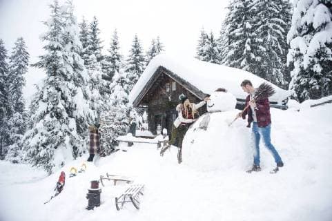 Austria, Altenmarkt-Zauchensee, friends building up big snowman at wooden house model released Symbolfoto property released  HHF05499
