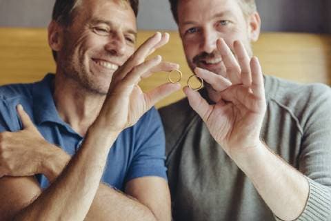 Happy gay couple holding up their wedding rings model released Symbolfoto property released  MFF03900