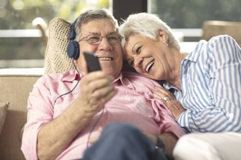 Happy senior couple with cell phone and headphones on couch at home model released Symbolfoto property released  ZEF14729