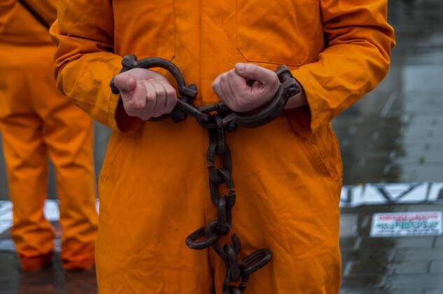 January 11, 2018 - London, UK. 11th January 2018. Protesters in orange jump suits and black hoods stand in a square at Trafalgar Square marking 16 years of the illegal detention and torture camp at Guantanamo Bay. The names of the 41 remaining detainees were read out, many held indefinitely without charge or trial, almost all who were sold to the US by Afghan militias and the Pakistani military for cash bounties with no real evidence of terrorist involvement, but whose torture in CIA secret prisons across the world before arrival at Guantanamo as while as throughout their detention there makes their release too embarrassing to US authorities. ImagesLive - ZUMAd99_ 20180111_zap_d99_026 Copyright: xPeterxMarshallx