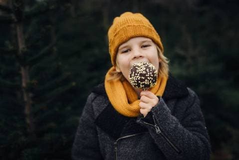 Little boy standing in front of fir trees, eating chocolate dipped apple model released Symbolfoto  MJF02241