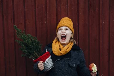 Laughing boy standing in front of wooden wall with potted Chritsmas tree and candied apple model released Symbolfoto  MJF02252