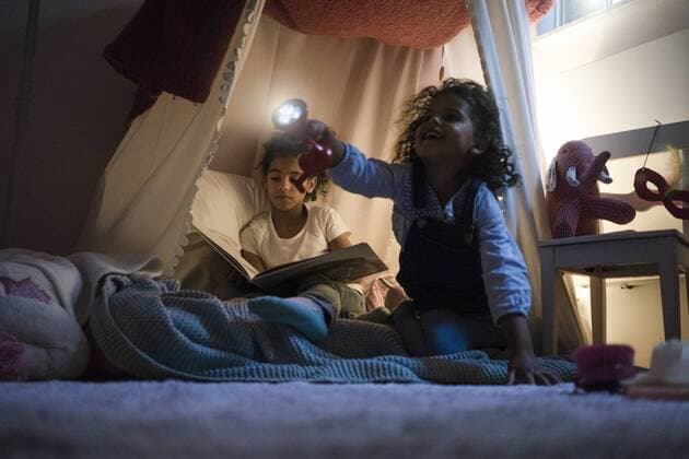 Two sisters sitting in dark children s room, playing with torch, reading book model released Symbolfoto property released  MOEF00336