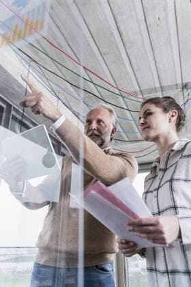 Casual mature businessman and young woman discussing data at glass pane in office model released Symbolfoto property released  UUF12776
