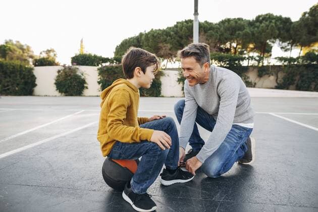 IMAGO Creative: Vaterschaft Father lacing son s shoe on basketball outdoor court model released Symbolfoto  EBSF02065