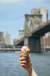 USA, New York, Brooklyn, Close up of woman hand holding a strawberry ice cream cone with Brooklyn Bridge in background model released Symbolfoto  DAPF00870