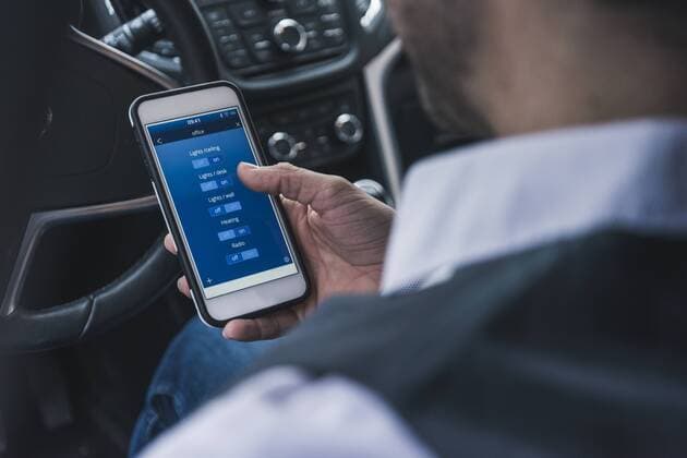 Man in car adjusting smart home devices via smartphone model released Symbolfoto property released  UUF12654